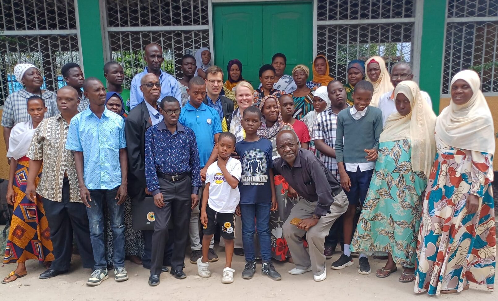 Iso joukko eri-ikäisiä ihmisiä katsoo kameraan. Suurin osa on afrikkalaisia, keskellä on kaksi vaaleaihoista, mies ja nainen.